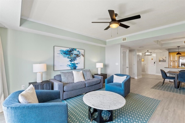 living room featuring ceiling fan with notable chandelier, hardwood / wood-style flooring, a tray ceiling, and crown molding