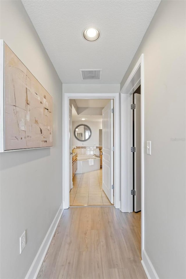 hallway with light hardwood / wood-style floors and a textured ceiling