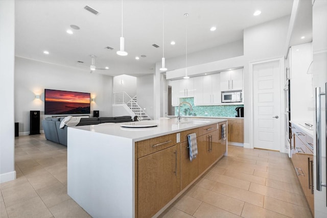 kitchen featuring white cabinets, a spacious island, sink, hanging light fixtures, and decorative backsplash