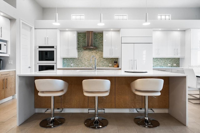 kitchen with white appliances, sink, wall chimney range hood, white cabinetry, and hanging light fixtures