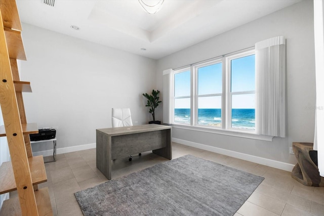 home office with a beach view, light tile patterned floors, a water view, and a raised ceiling