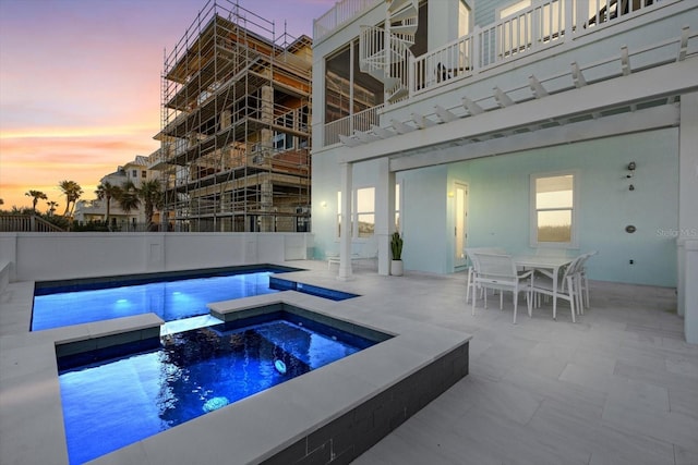 pool at dusk with a pergola, an in ground hot tub, and a patio