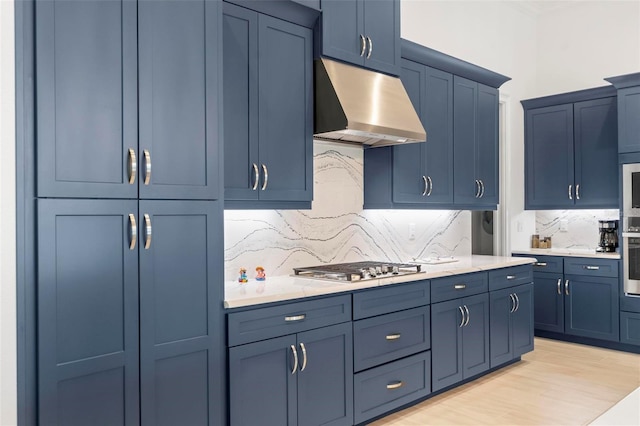 kitchen featuring appliances with stainless steel finishes, blue cabinets, light wood-type flooring, and backsplash