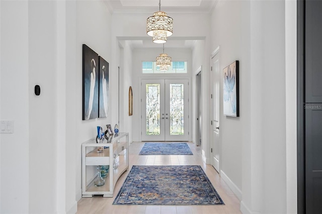 foyer with a high ceiling, crown molding, light hardwood / wood-style floors, and french doors