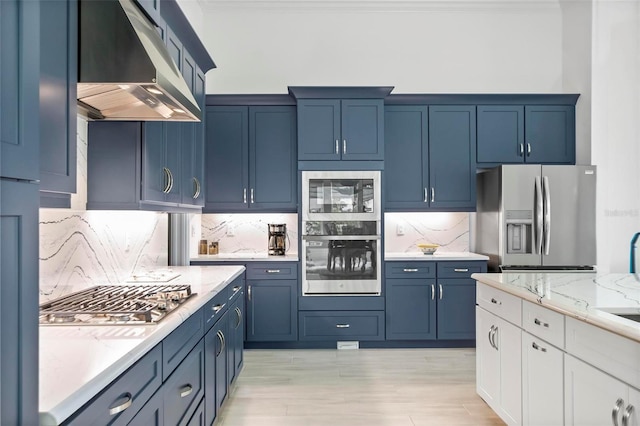 kitchen with tasteful backsplash, appliances with stainless steel finishes, blue cabinetry, and light stone counters