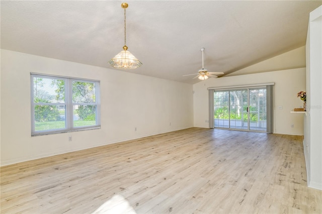 empty room with lofted ceiling, a healthy amount of sunlight, light hardwood / wood-style floors, and ceiling fan with notable chandelier