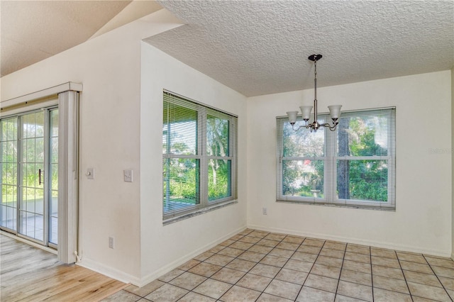 unfurnished dining area with light tile patterned floors, a textured ceiling, and an inviting chandelier