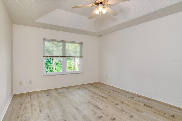 spare room with a textured ceiling, a tray ceiling, light hardwood / wood-style flooring, and ceiling fan