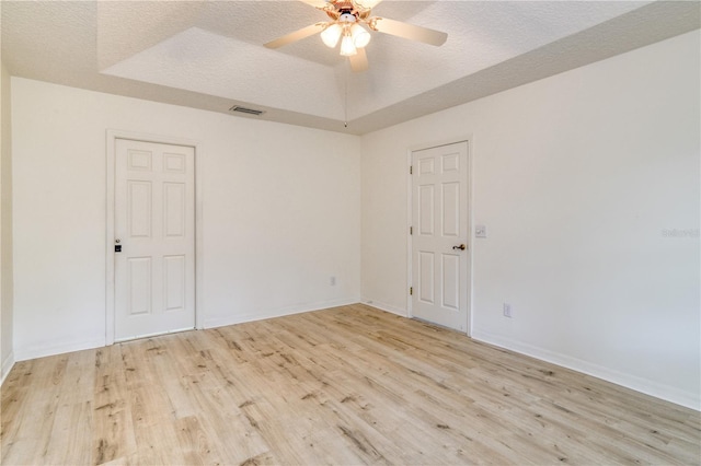 spare room with ceiling fan, a raised ceiling, light wood-type flooring, and a textured ceiling