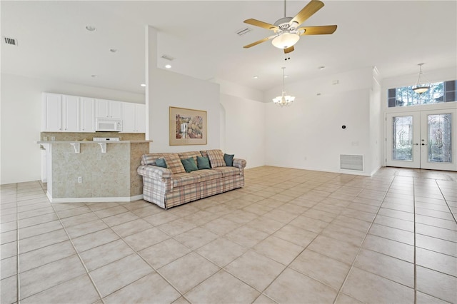 tiled living room with ceiling fan with notable chandelier, a high ceiling, and french doors