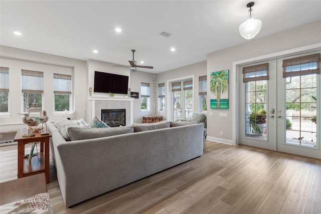 living area featuring french doors, recessed lighting, visible vents, a glass covered fireplace, and light wood-type flooring