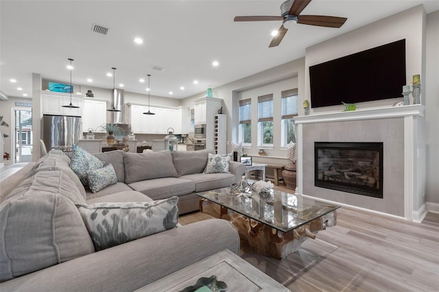 living area featuring a tile fireplace, light wood-style flooring, recessed lighting, visible vents, and baseboards