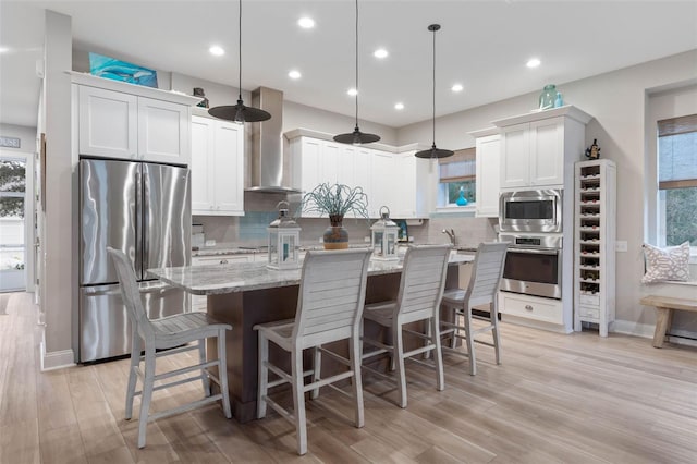 kitchen featuring wine cooler, a center island, appliances with stainless steel finishes, light stone countertops, and wall chimney exhaust hood