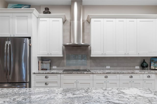 kitchen featuring black electric cooktop, white cabinets, wall chimney range hood, backsplash, and freestanding refrigerator