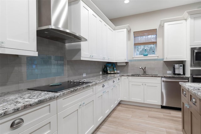 kitchen featuring a sink, white cabinetry, appliances with stainless steel finishes, wall chimney exhaust hood, and tasteful backsplash