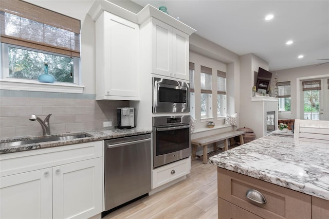 kitchen featuring light wood-style flooring, a sink, white cabinetry, appliances with stainless steel finishes, and light stone countertops