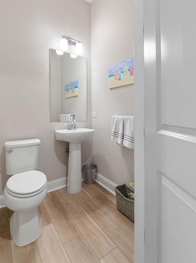 bathroom with toilet, a sink, baseboards, and wood finished floors