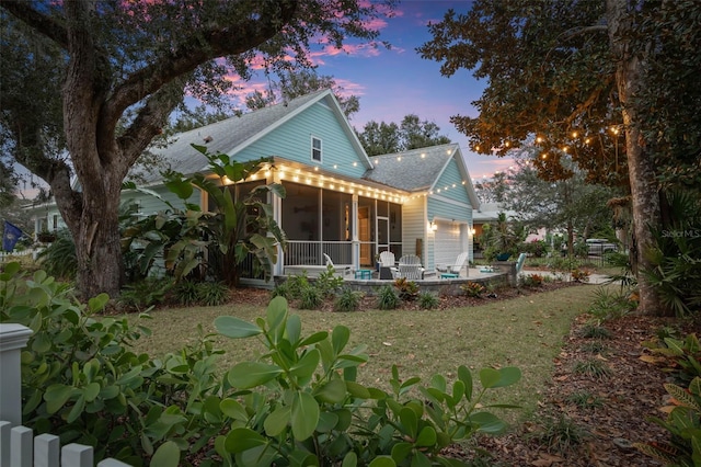 back of house at dusk with a garage, a sunroom, and roof with shingles