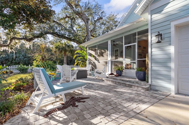 view of patio / terrace featuring a garage, outdoor dining space, fence, and a sunroom