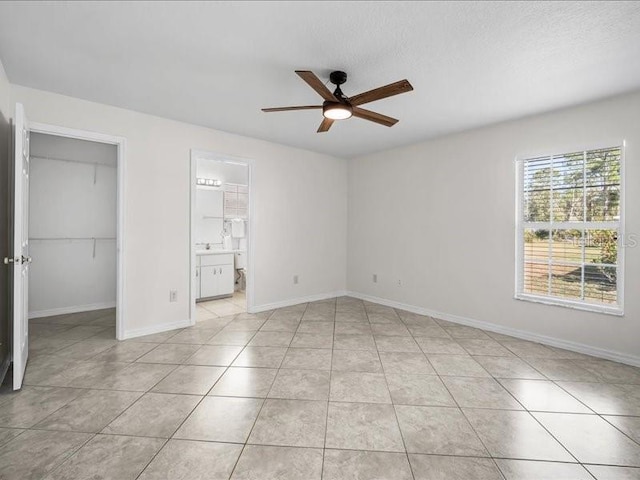 unfurnished bedroom with ensuite bath, a spacious closet, ceiling fan, a closet, and light tile patterned flooring