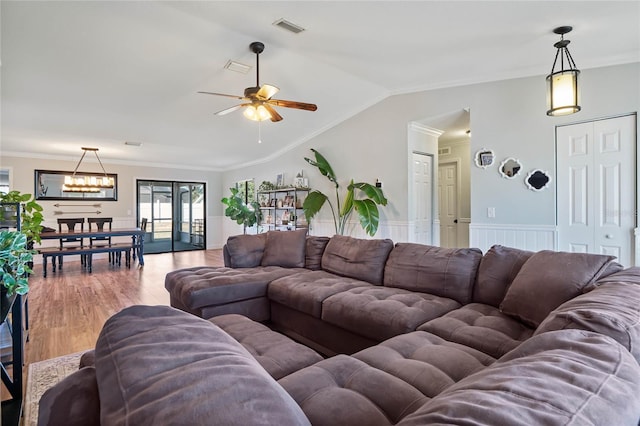 living room featuring lofted ceiling, crown molding, wood-type flooring, and ceiling fan with notable chandelier