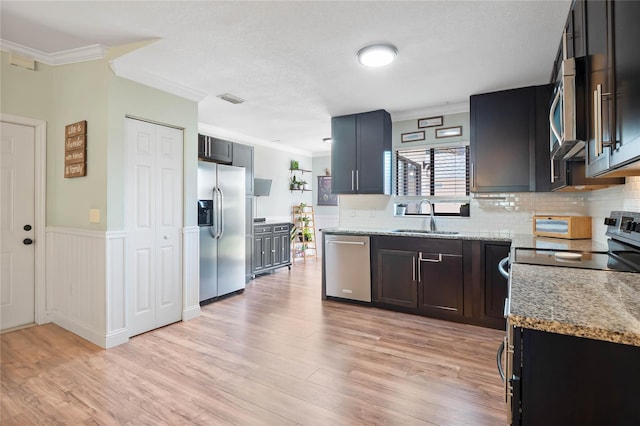 kitchen featuring light stone countertops, sink, crown molding, light hardwood / wood-style floors, and appliances with stainless steel finishes