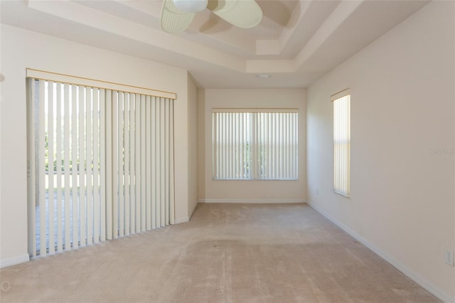 unfurnished room featuring a raised ceiling, ceiling fan, and light colored carpet