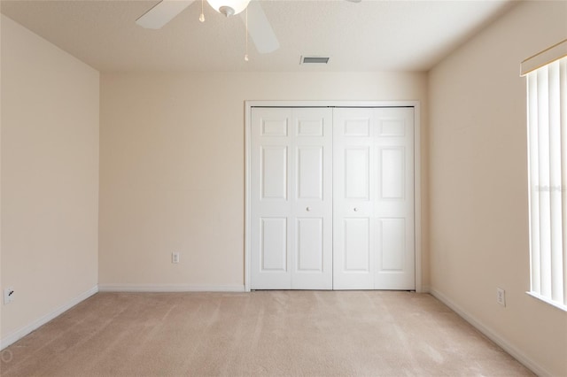 unfurnished bedroom with a closet, multiple windows, light colored carpet, and ceiling fan