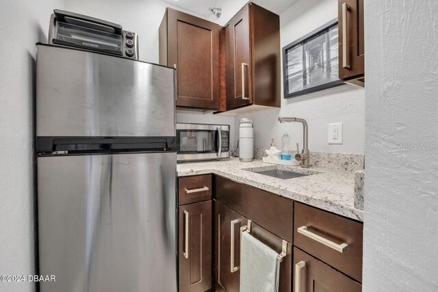 kitchen featuring sink, light stone countertops, stainless steel appliances, and dark brown cabinetry