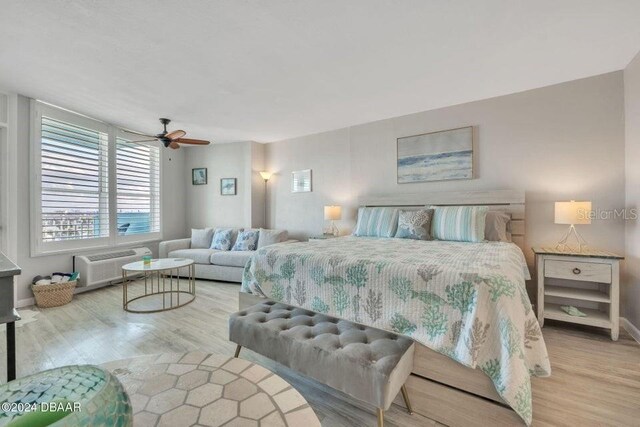 bedroom featuring a wall unit AC, ceiling fan, and light hardwood / wood-style flooring