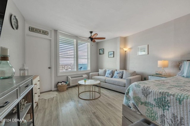 bedroom featuring ceiling fan, a wall mounted AC, and light hardwood / wood-style flooring