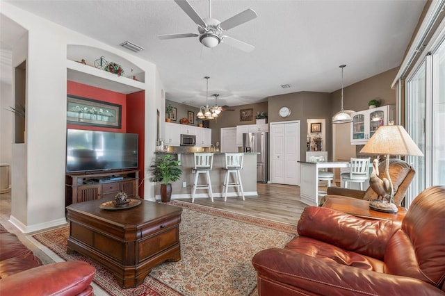 living room featuring ceiling fan with notable chandelier, light wood-type flooring, and a textured ceiling