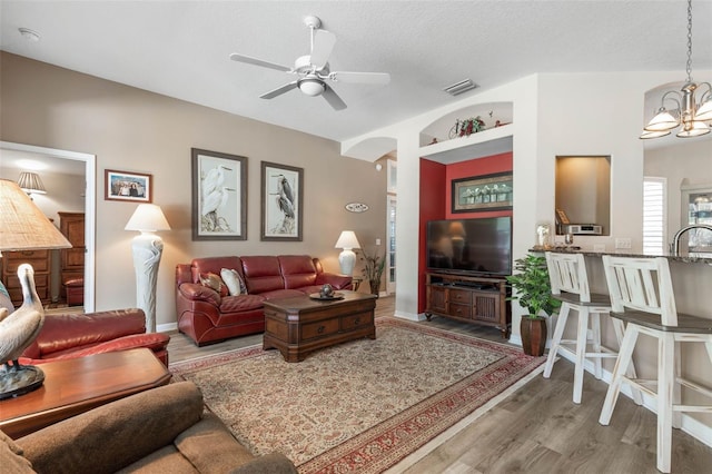 living room with sink, ceiling fan with notable chandelier, a textured ceiling, and hardwood / wood-style flooring