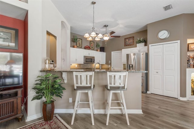 kitchen with white cabinets, appliances with stainless steel finishes, kitchen peninsula, and hanging light fixtures