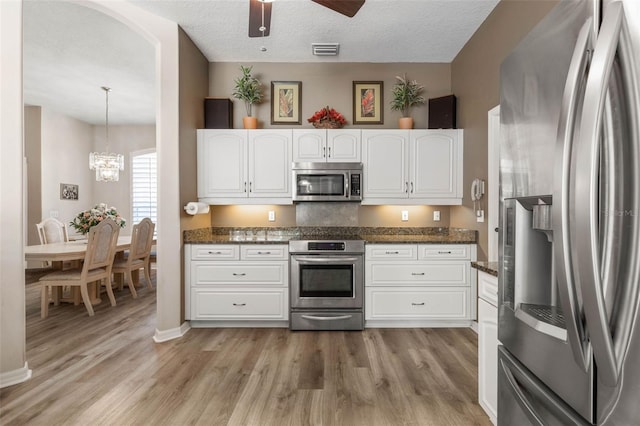 kitchen with white cabinetry, hanging light fixtures, dark stone countertops, light hardwood / wood-style floors, and appliances with stainless steel finishes