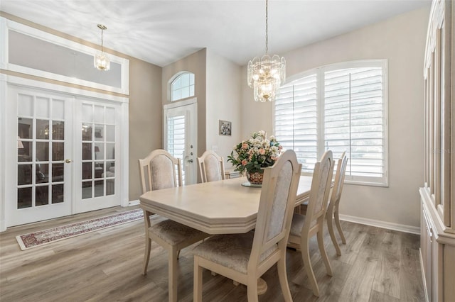 dining space with french doors, light hardwood / wood-style floors, plenty of natural light, and a notable chandelier