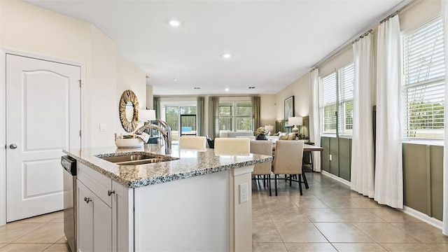 kitchen with light stone countertops, white cabinetry, sink, and an island with sink