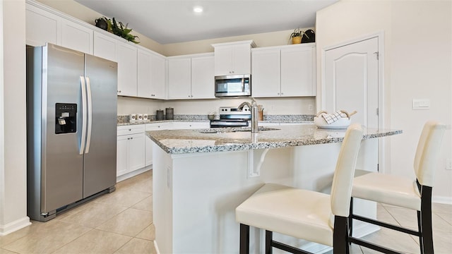 kitchen featuring white cabinets, appliances with stainless steel finishes, a breakfast bar, and light stone countertops