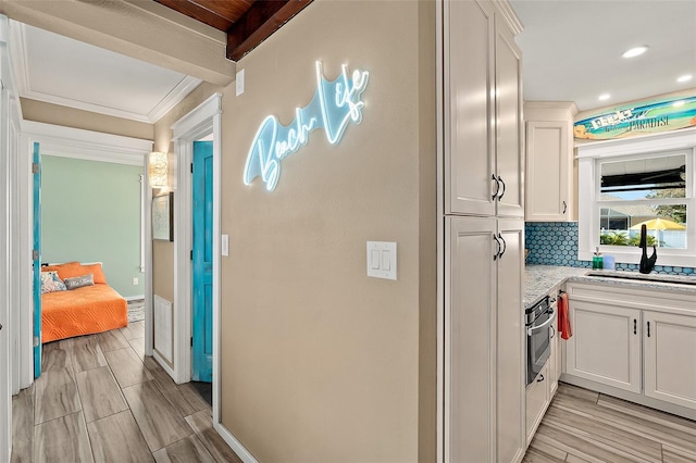 hall featuring beamed ceiling, crown molding, and sink