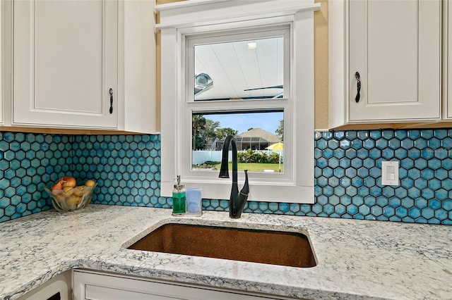 kitchen with tasteful backsplash, light stone counters, sink, and white cabinets