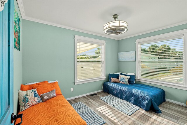 bedroom featuring light wood-type flooring, multiple windows, and crown molding