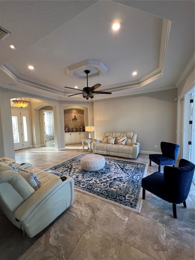 living room with a tray ceiling, crown molding, and ceiling fan