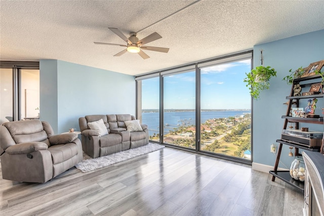 living room featuring a water view, ceiling fan, light wood-type flooring, a textured ceiling, and a wall of windows