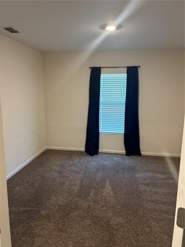 empty room with dark colored carpet, visible vents, and baseboards