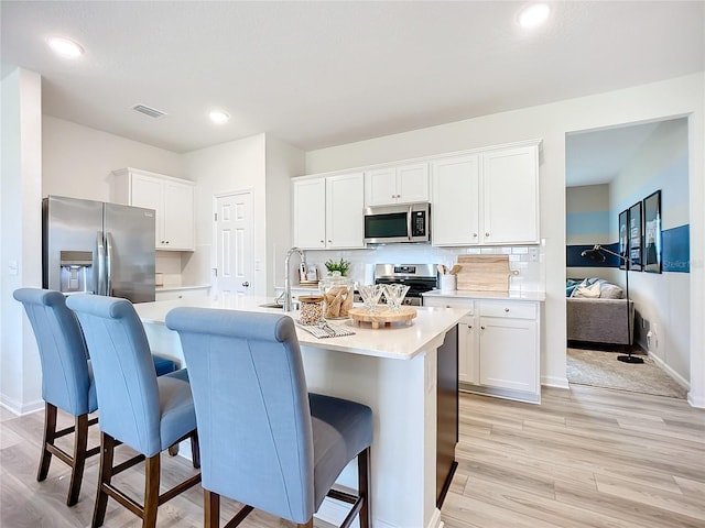 kitchen with appliances with stainless steel finishes, light hardwood / wood-style flooring, white cabinetry, and an island with sink