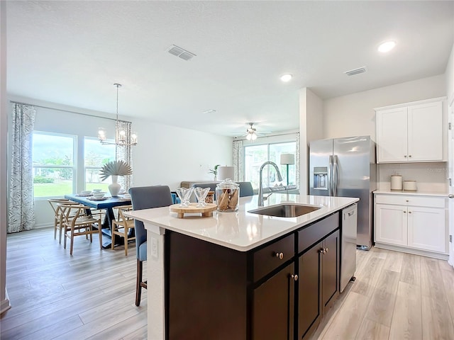 kitchen featuring ceiling fan with notable chandelier, sink, light hardwood / wood-style flooring, a kitchen bar, and white cabinetry