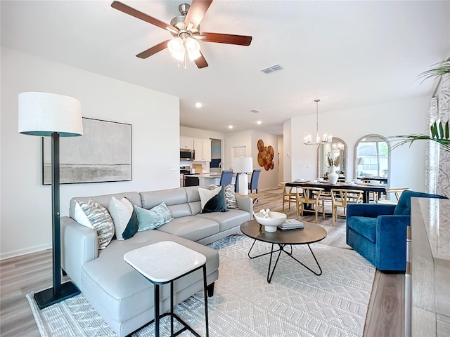 living room featuring ceiling fan with notable chandelier and light hardwood / wood-style floors