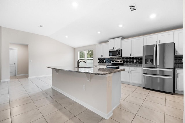 kitchen featuring lofted ceiling, a kitchen island with sink, sink, dark stone countertops, and appliances with stainless steel finishes