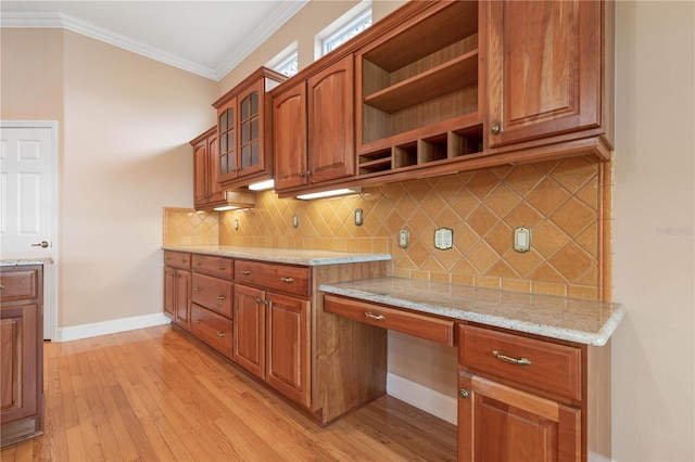 kitchen with crown molding, light hardwood / wood-style flooring, built in desk, light stone countertops, and tasteful backsplash