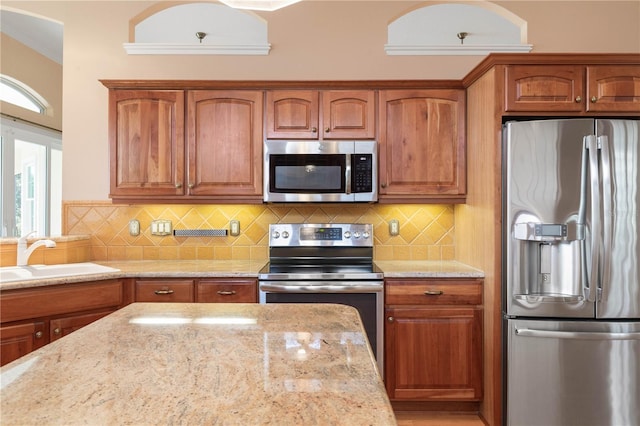 kitchen with light stone countertops, decorative backsplash, stainless steel appliances, and sink